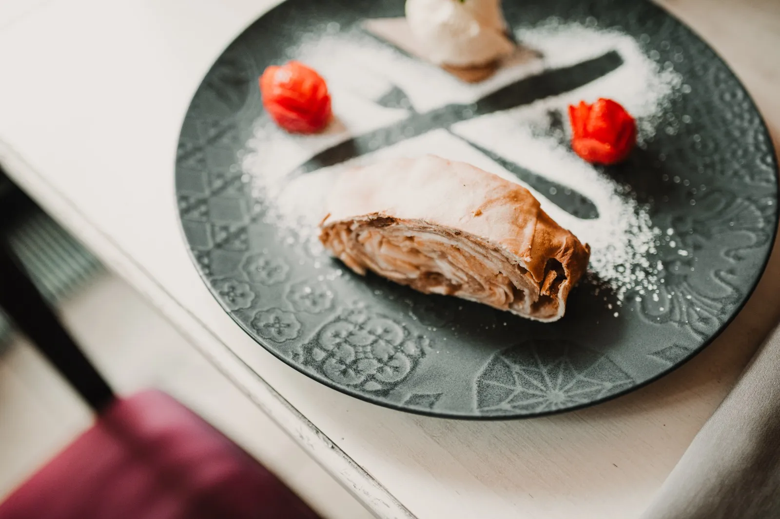 Apfelstrudel mit Puderzucker und Erdbeeren auf grauem Teller